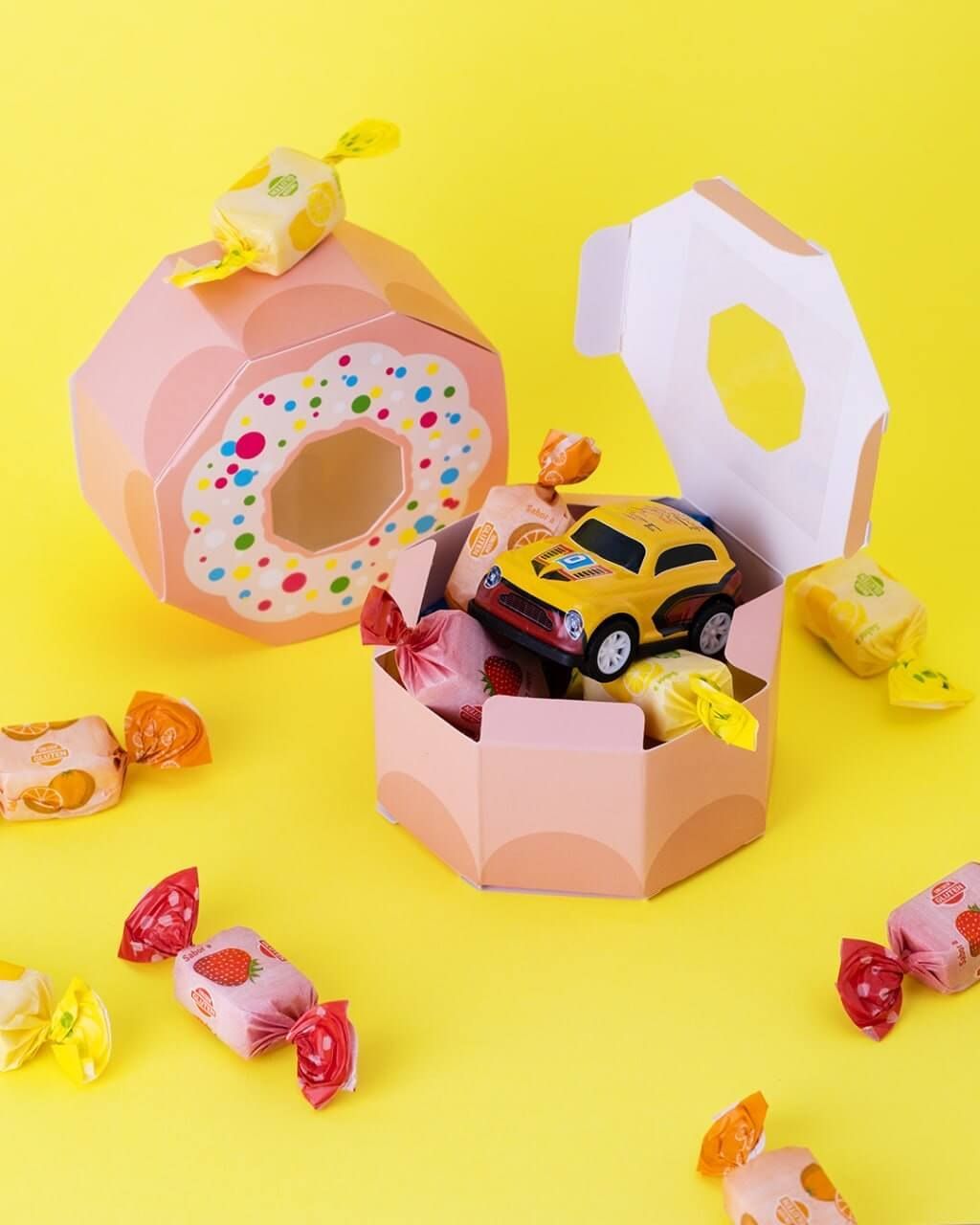 Una caja con forma de dona llena de dulces y un coche de juguete.