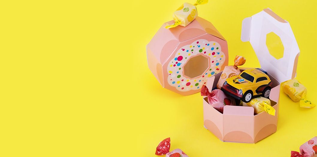 Una caja rosa con forma de dona llena de dulces y un carrito de juguete.