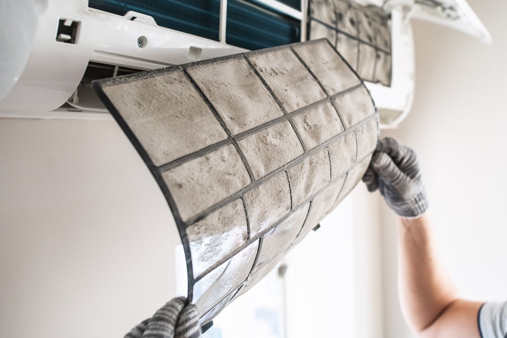 Grant technician looking at dirty air filter in mini split duct during a Mississippi summer.