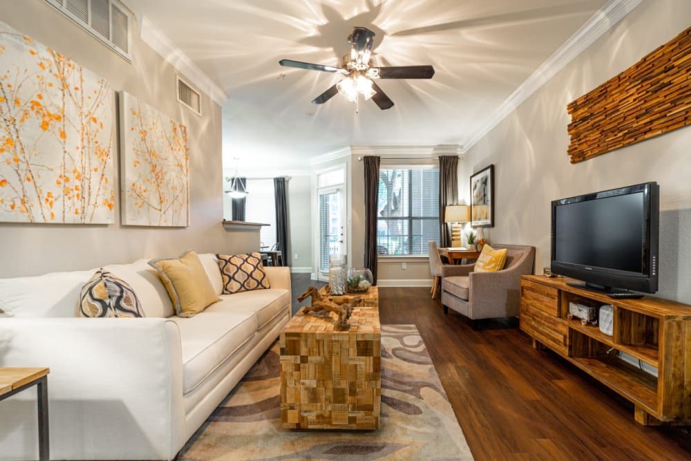 a living room with a couch, chair, coffee table, television, and ceiling fan at Marquis at Great Hills in Austin, TX.