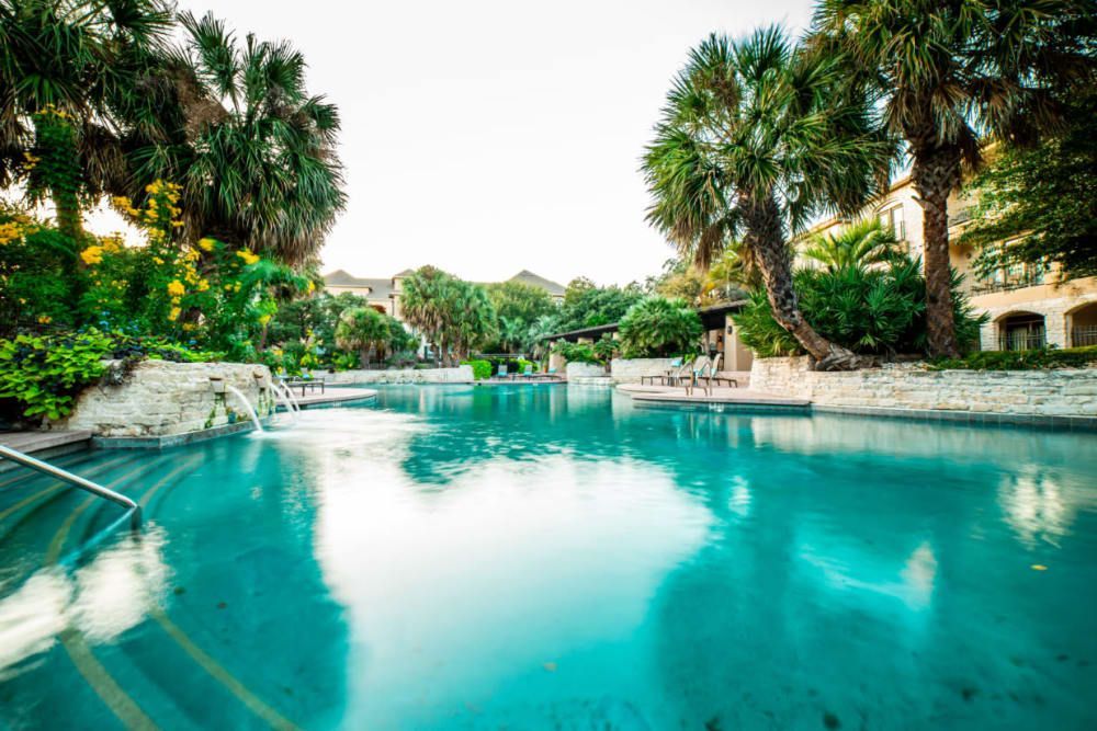 a large swimming pool surrounded by palm trees and a building at Marquis at Great Hills in Austin, TX.
