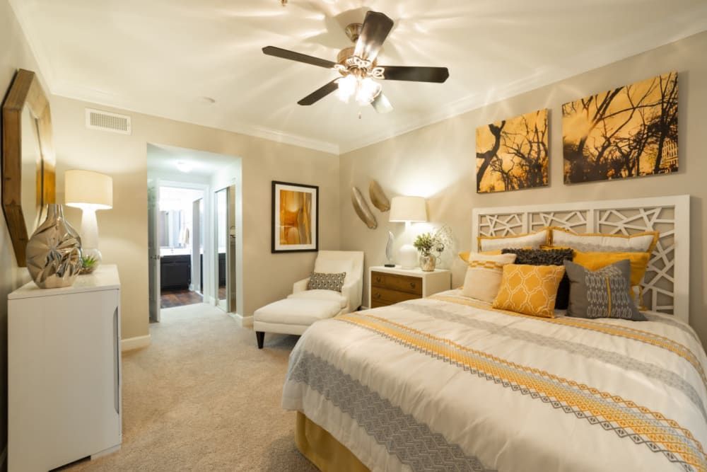 a bedroom with a bed, chair, nightstand, and ceiling fan at Marquis at Great Hills in Austin, TX.