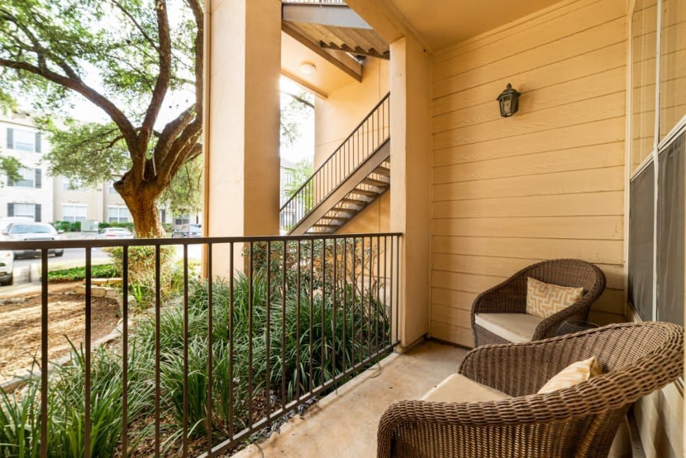 a balcony with two chairs and a table with a tree in the background at Marquis at Great Hills in Austin, TX.