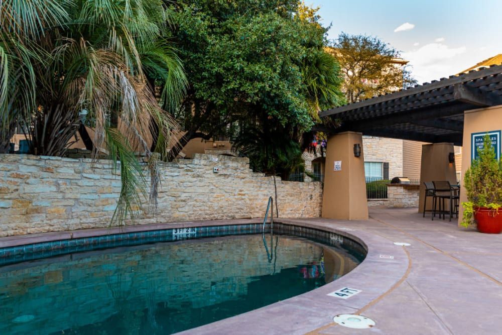 a large swimming pool is surrounded by trees and a stone wall at Marquis at Great Hills in Austin, TX.