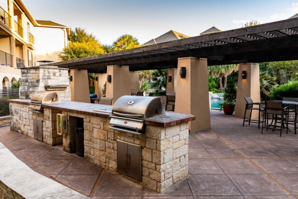 a large outdoor kitchen with a grill and tables under a canopy at Marquis at Great Hills in Austin, TX.