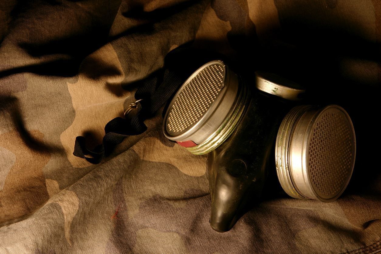 A gas mask is laying on a blanket on a bed.