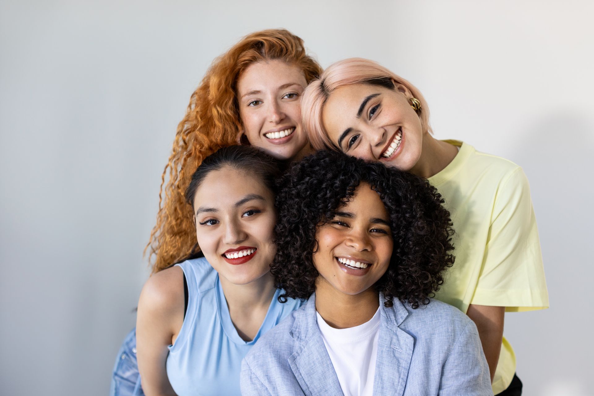 Four smiling people of diverse appearance posing together against a light background.
