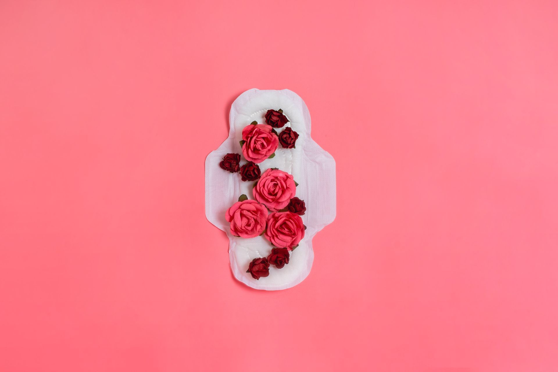 Sanitary pad decorated with red and pink flowers on a pink background.