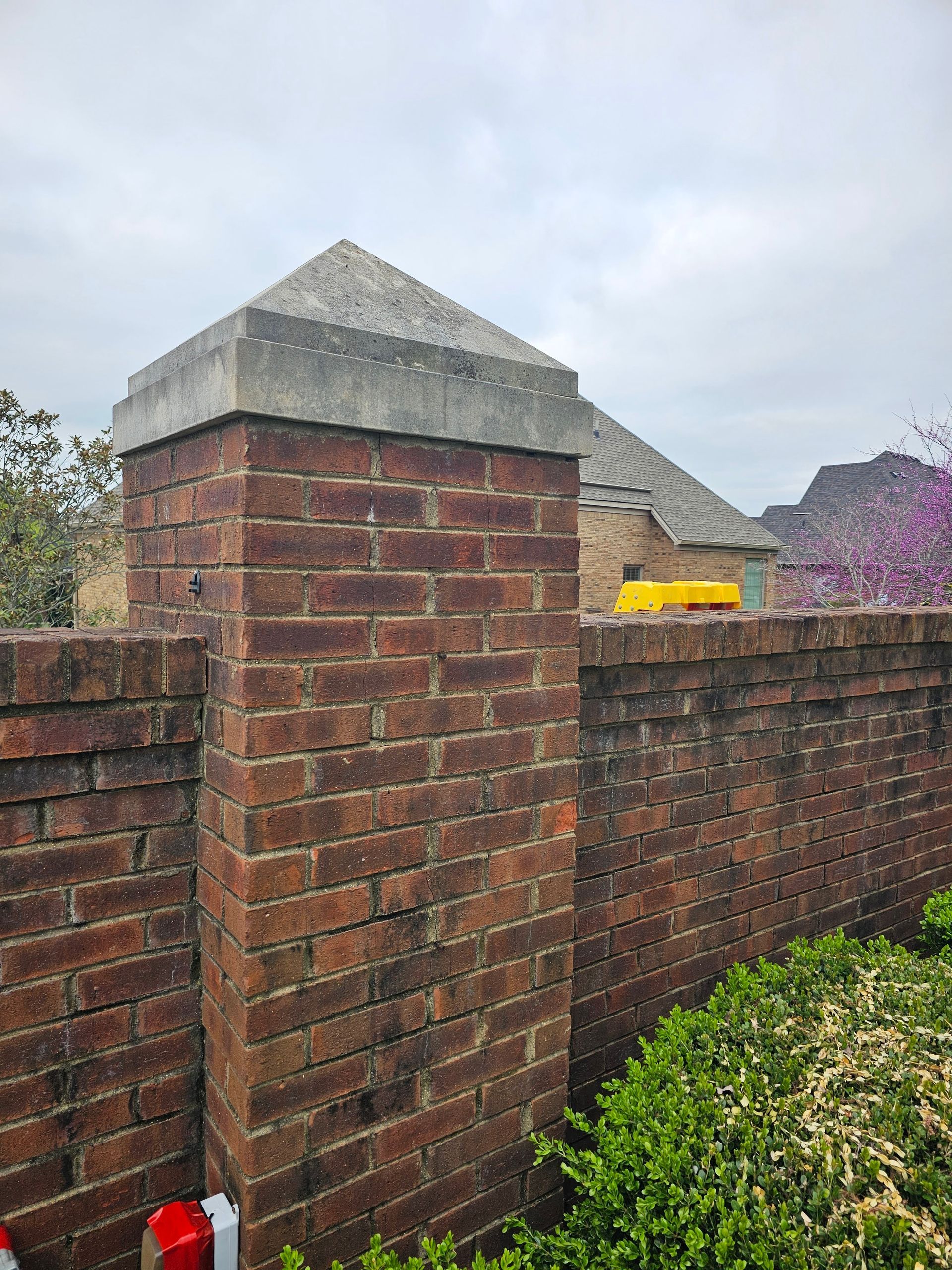 Brick pillar topped with concrete, part of a wall in front of a house, cloudy day.