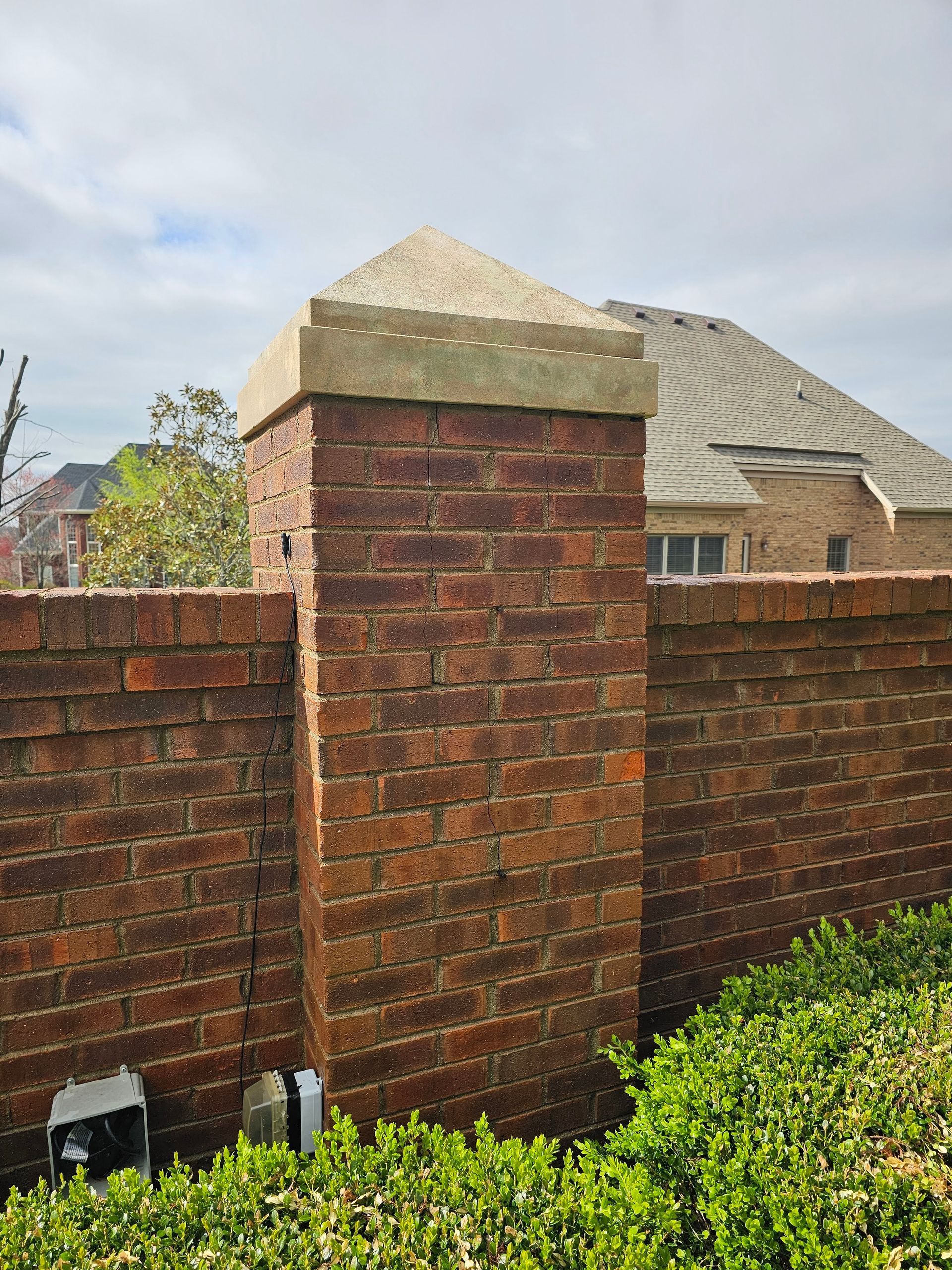 Brick pillar with a concrete cap on a brick wall, with a building in the background.