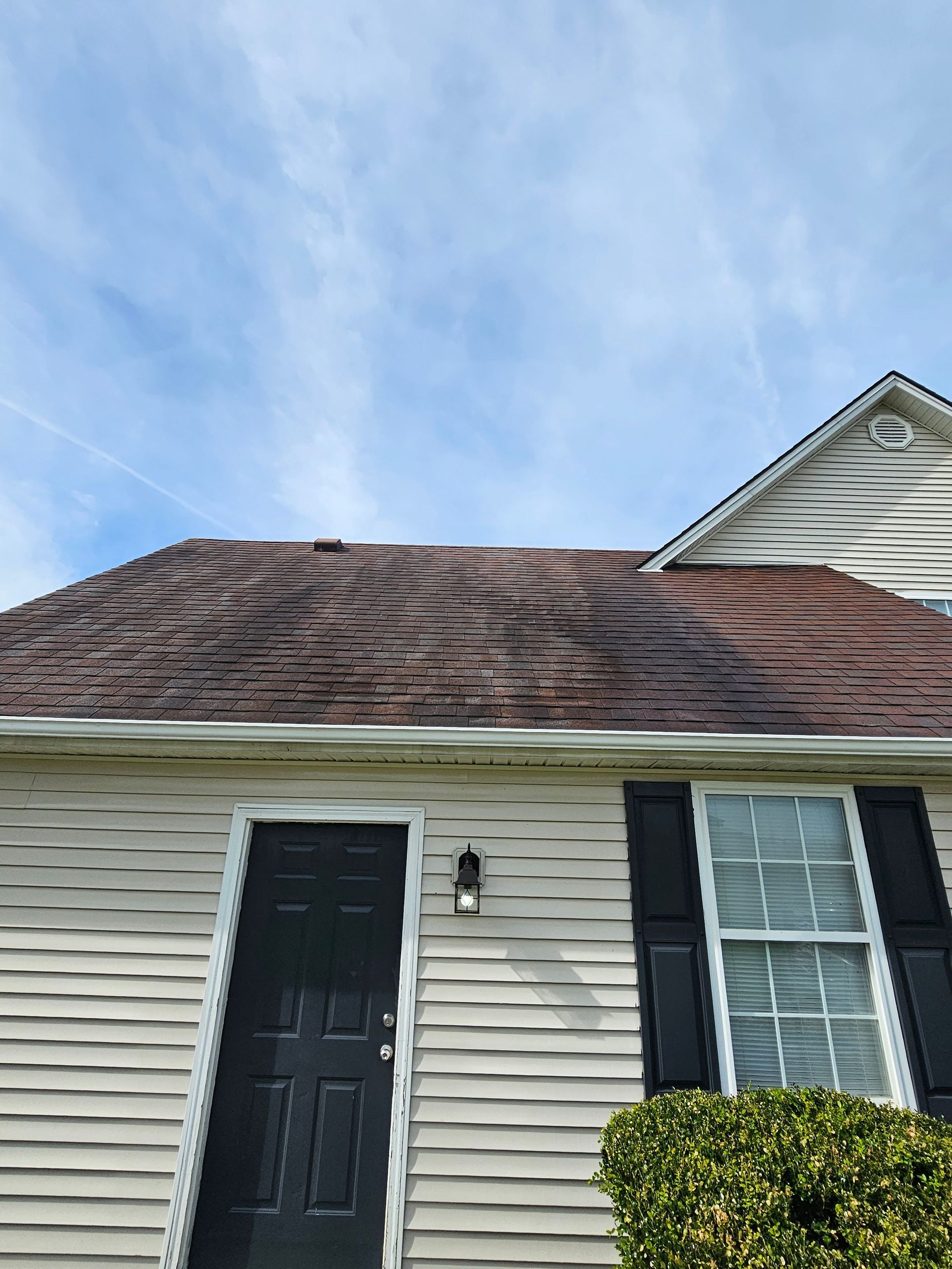 Brown shingled roof and cream siding home with black door and shutters against a blue sky.