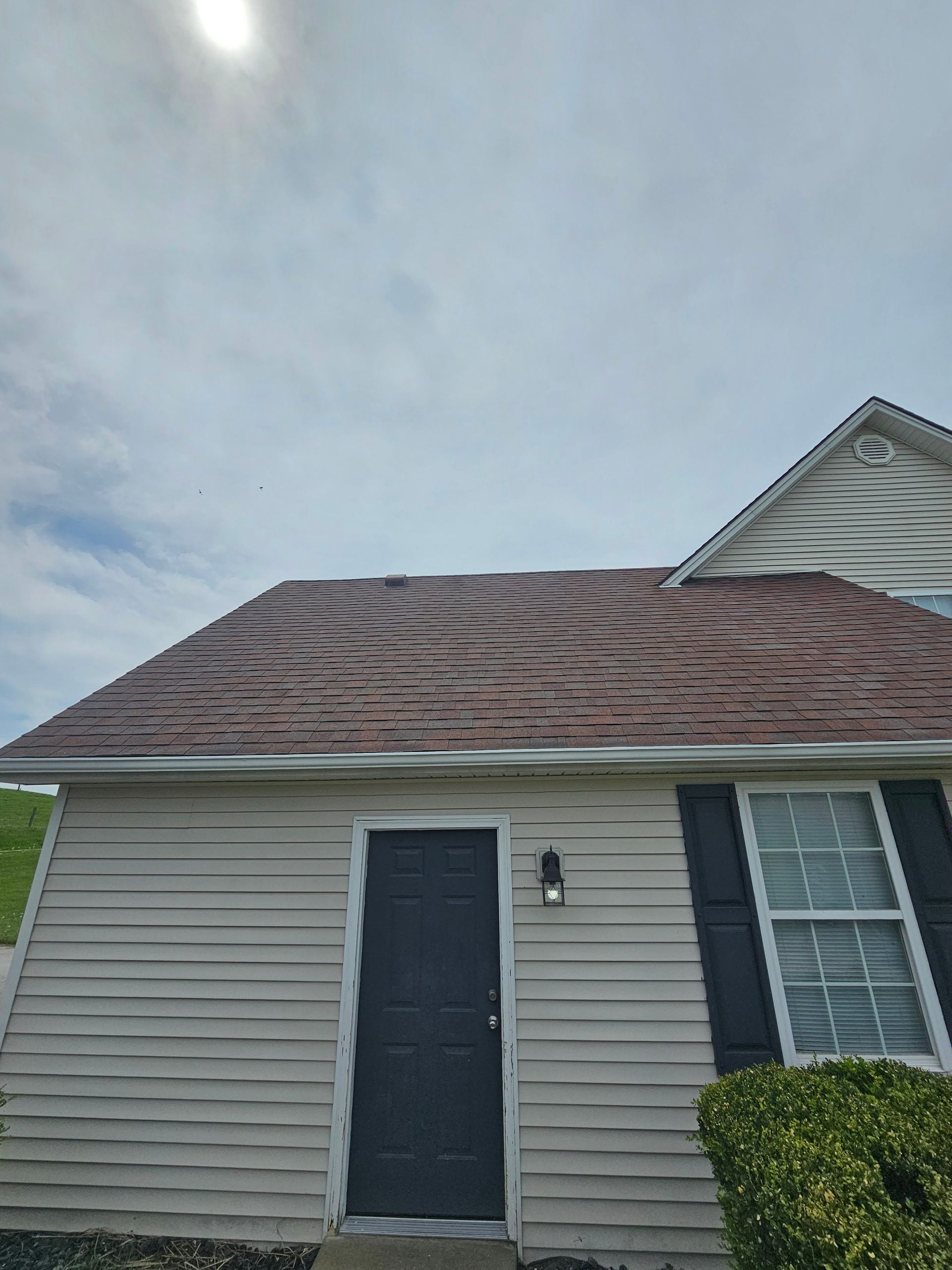 Tan house with dark roof and door, white trim, and a cloudy sky.