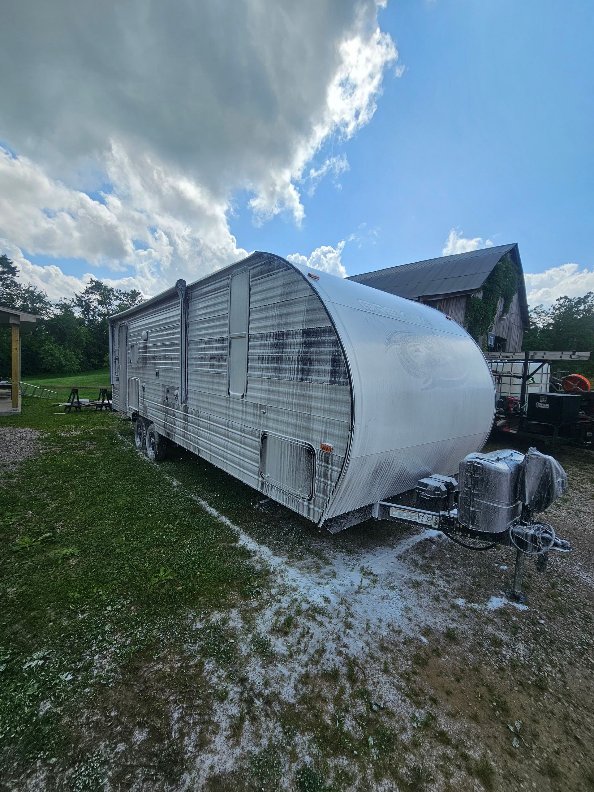 Camper trailer covered in white foam, parked on grass, blue sky background.