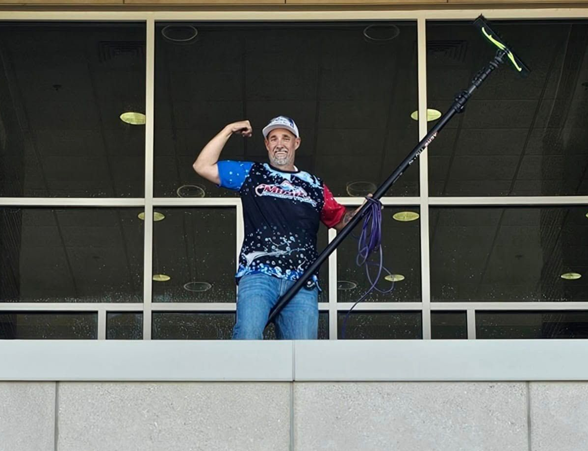 Man flexing arm, holding window washing tool, standing in front of window.