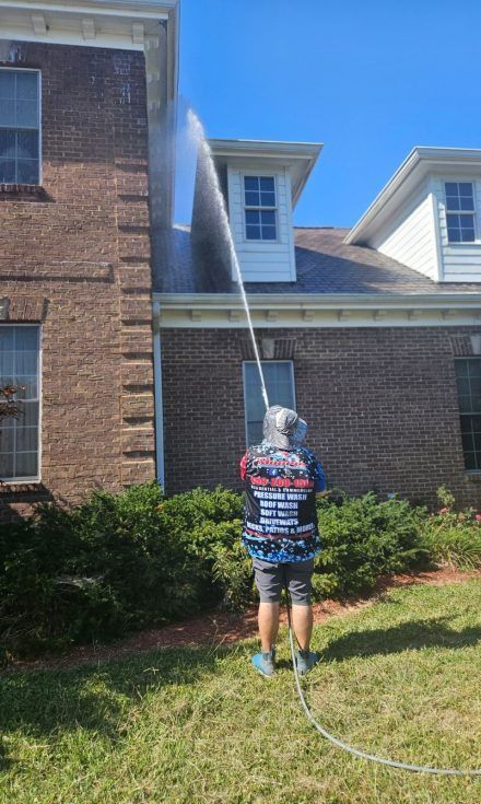 Person power washing a brick house roof on a sunny day.
