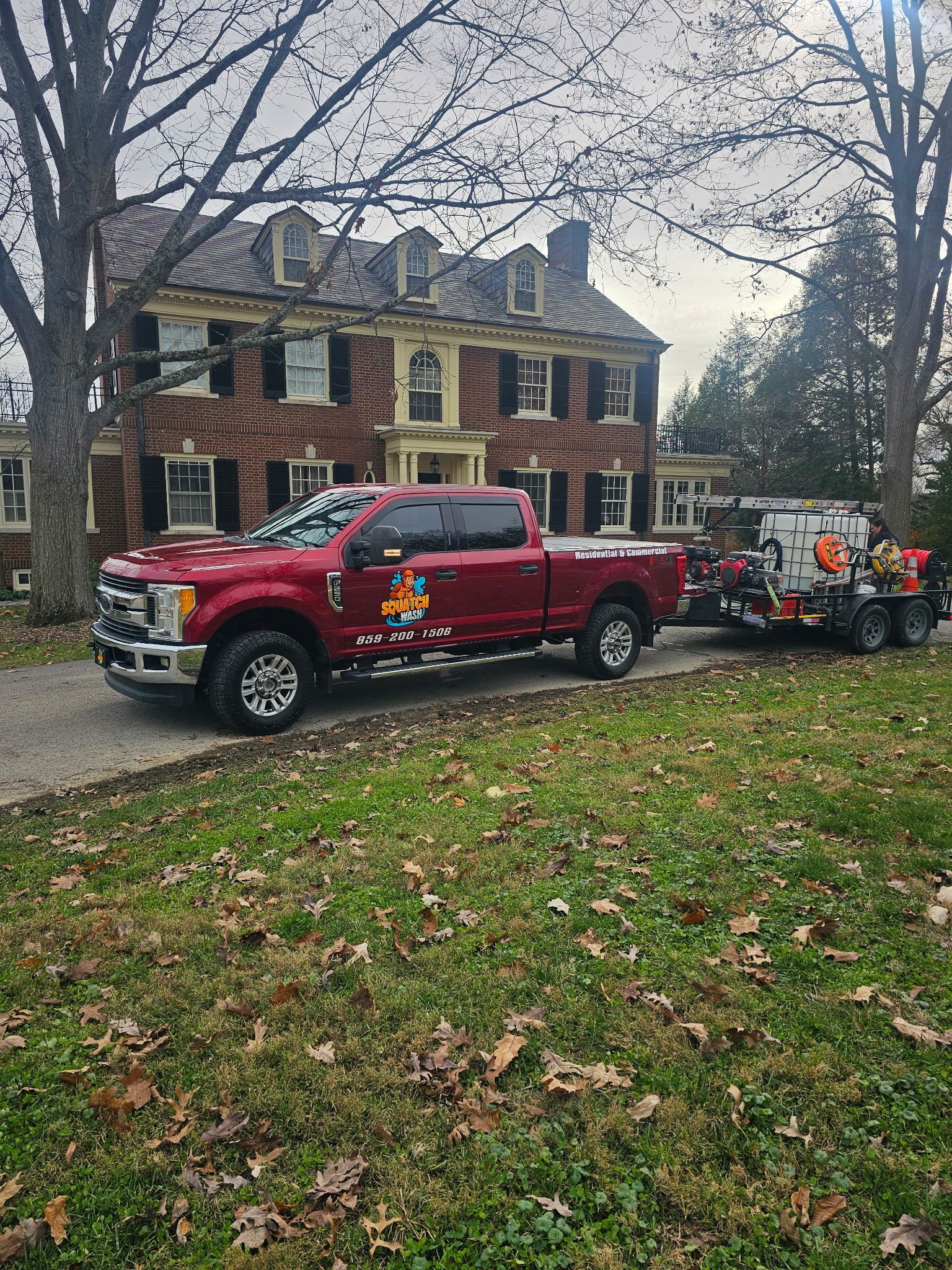 A gray pickup truck towing a trailer with water tanks spraying a house on a suburban street.