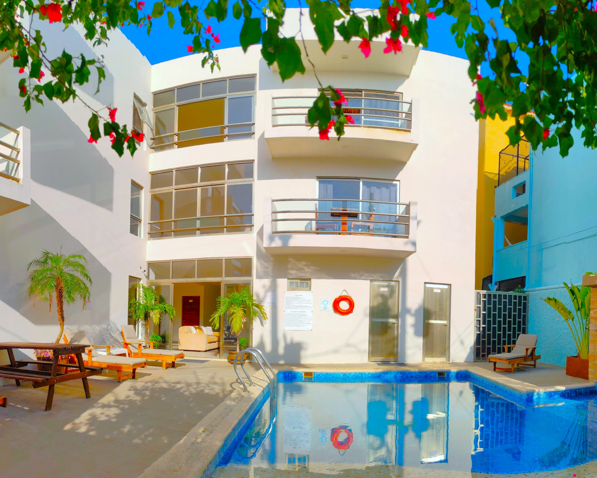 Hotel Arrecifes exterior , Edificio blanco con piscina y tumbonas, árboles y flores contra un cielo azul.