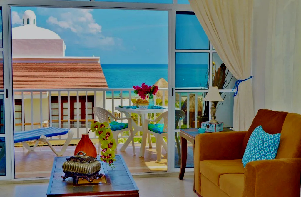 Sala de estar con vista al mar y balcón, con sofá, mesa y flores.