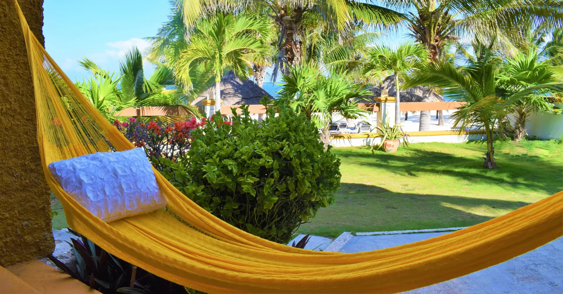 Hamaca amarilla con almohada blanca, con vista a un exuberante patio verde y al mar.
