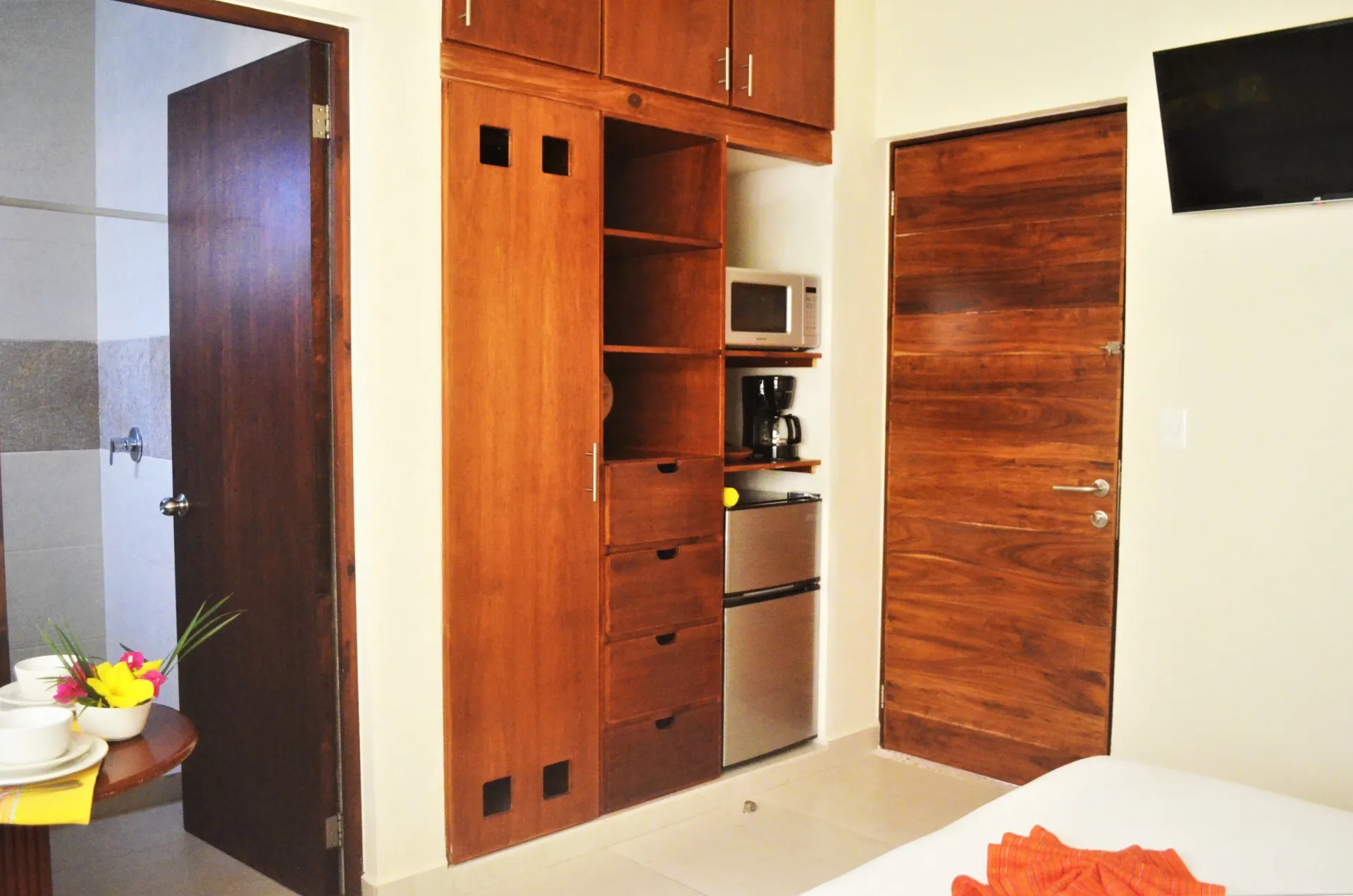 Armario de madera con mininevera, microondas y cafetera, con puerta de baño y puerta de habitación.