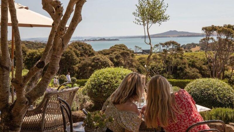 Two women are sitting at a table with a view of the ocean from Mudbrick Winery