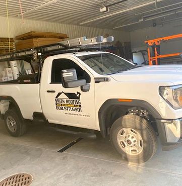 A white truck is parked in a garage with a ladder on top of it.