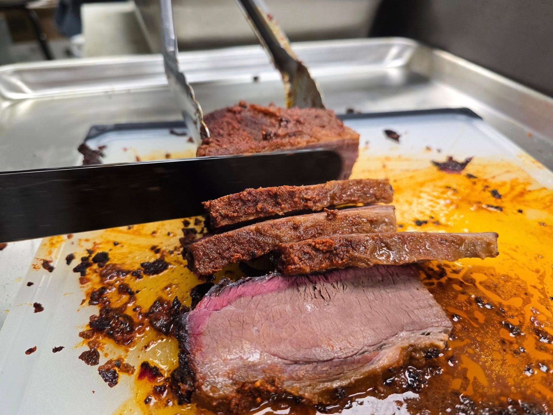 A person cutting a piece of seasoned, roasted meat on a white cutting board.