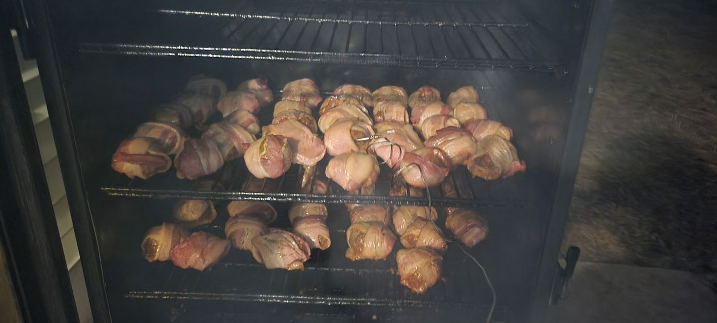 Bacon-wrapped meat smoking in a dark smoker with two racks.