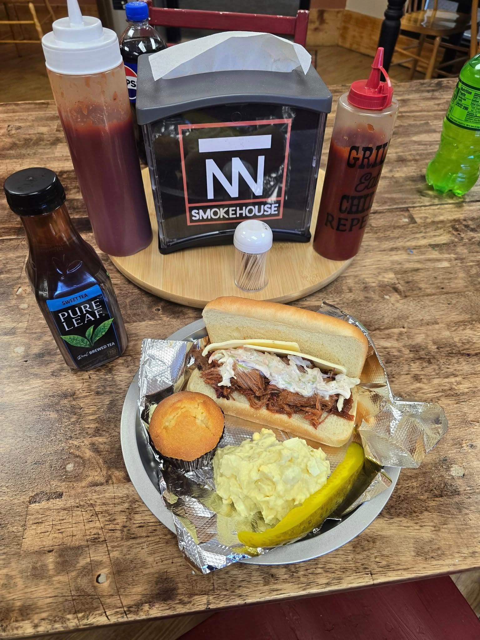 Barbecue sandwich with sides, sauces, and drinks on a table; restaurant setting.