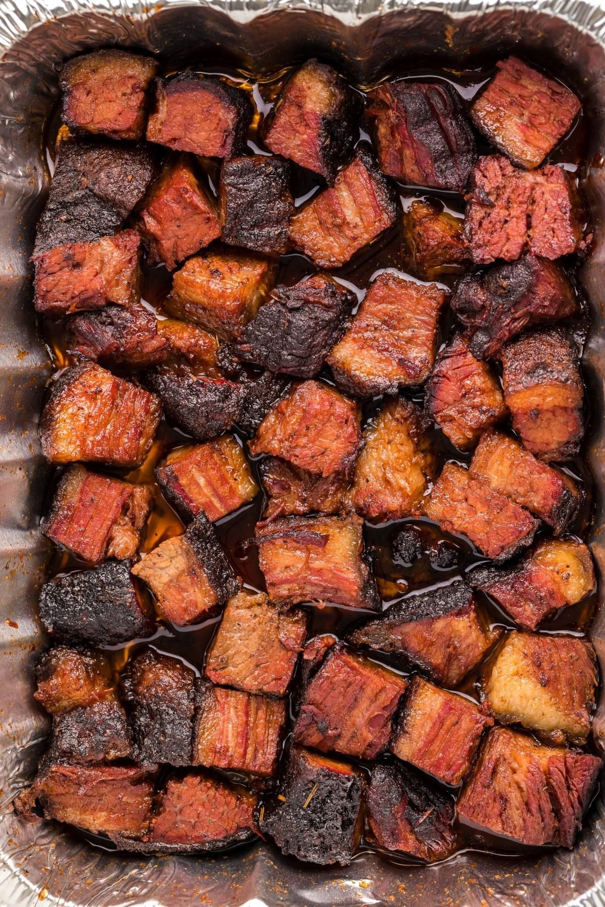 Smoked brisket burnt ends in a foil pan, with a dark, caramelized exterior and reddish-brown interior.