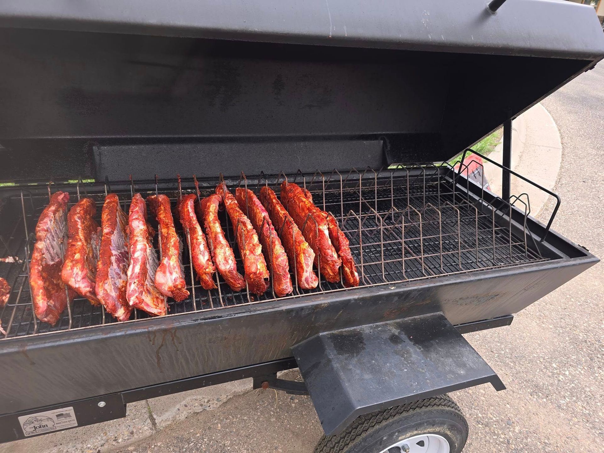 Smoked ribs on a black grill, outdoors. The ribs are seasoned and red.