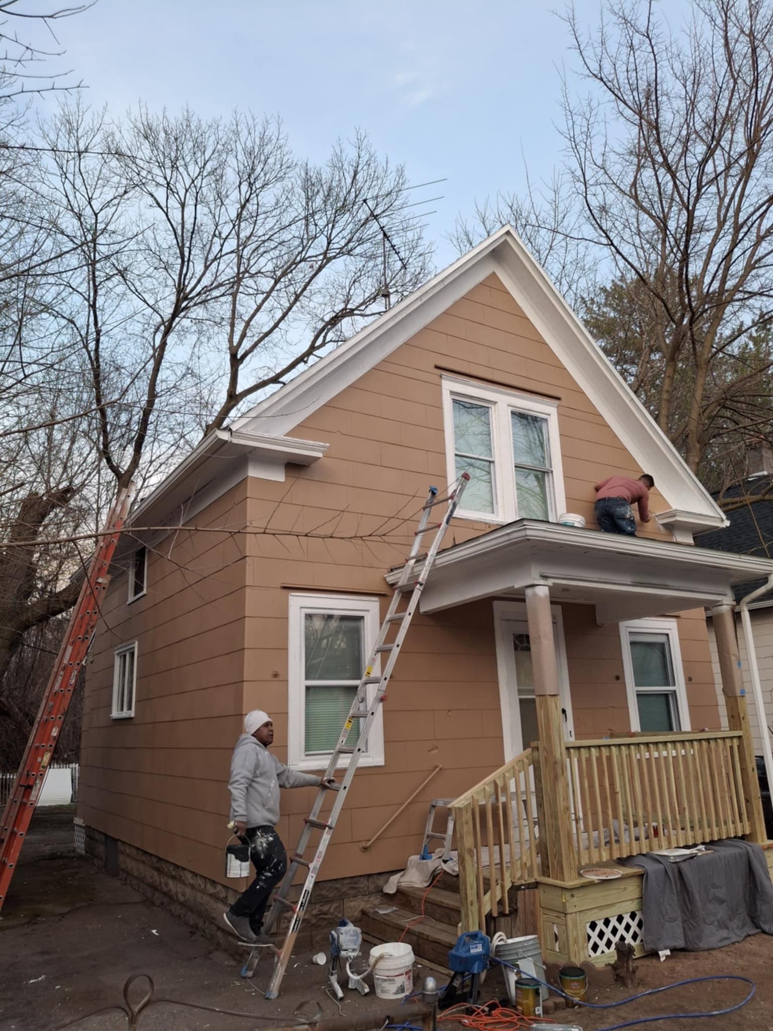 A man is standing on a ladder in front of a house being painted.