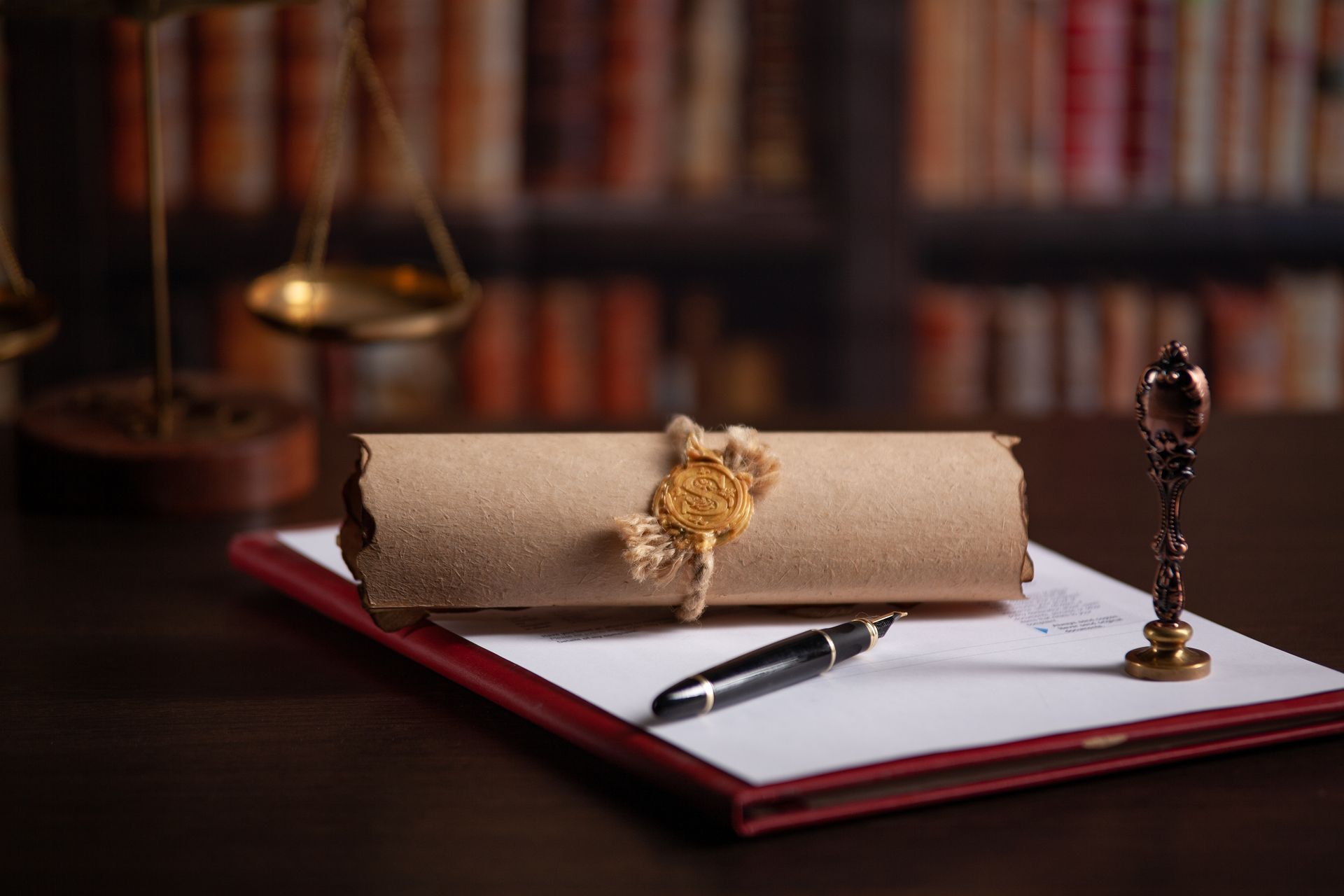 Legal documents on a desk: scroll, wax seal, pen, notepad, and scales of justice.