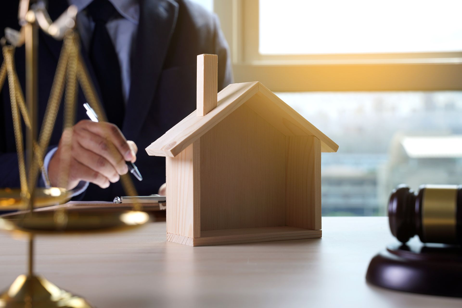 Lawyer reviewing paperwork next to a model house, scales, and gavel.