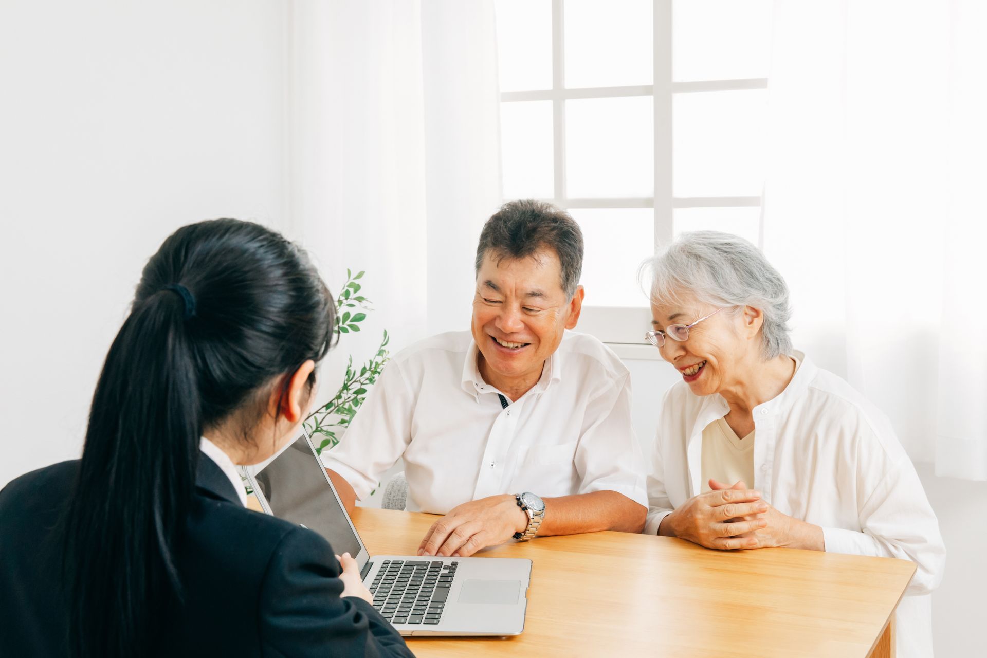 Woman in suit showing laptop to smiling older couple at table.