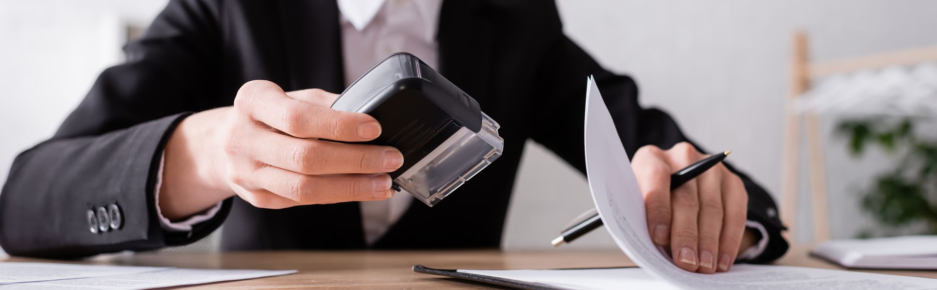 Person in suit holding a stamp over a document, with a pen in the other hand.