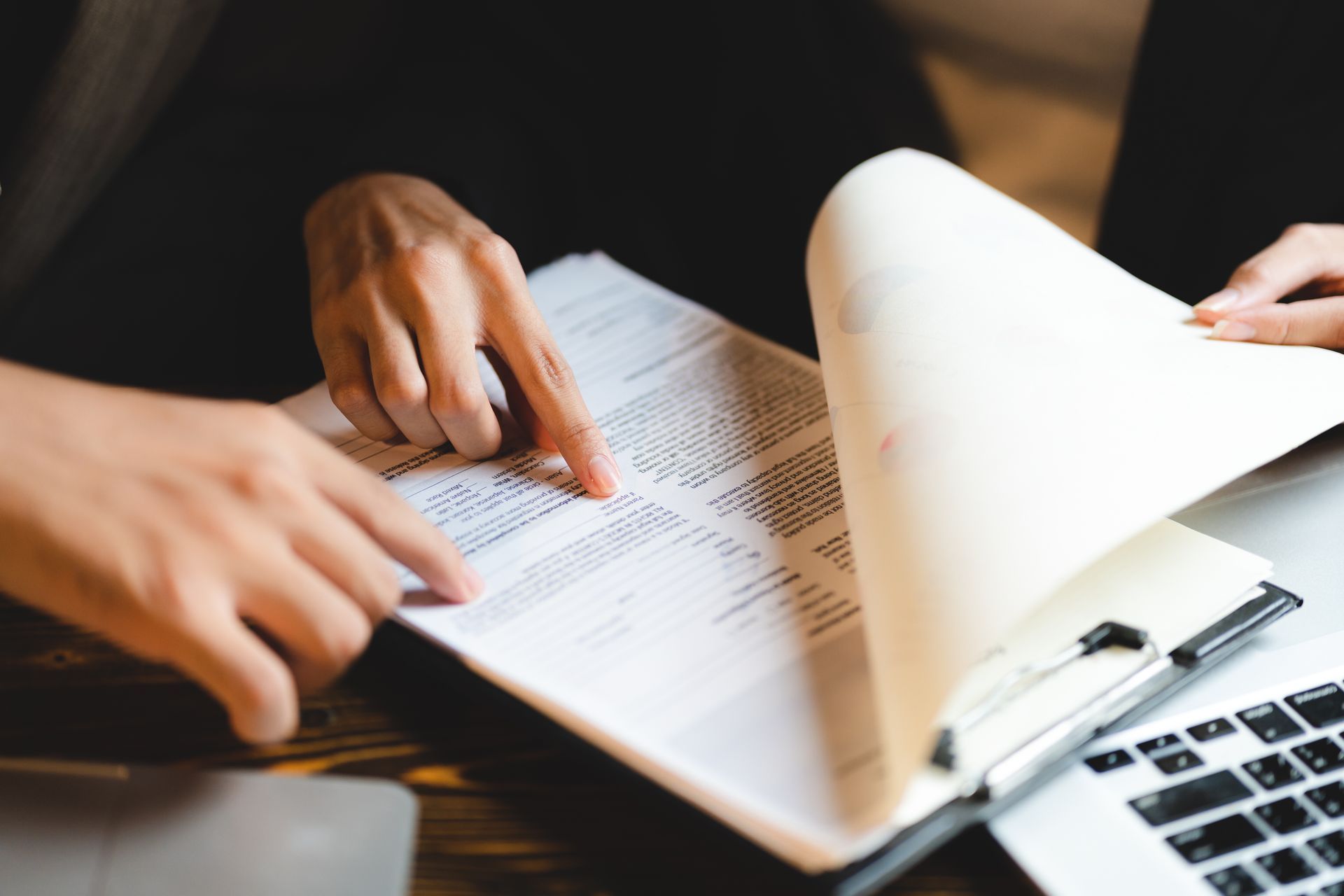 Hands pointing to document on a clipboard next to a laptop.