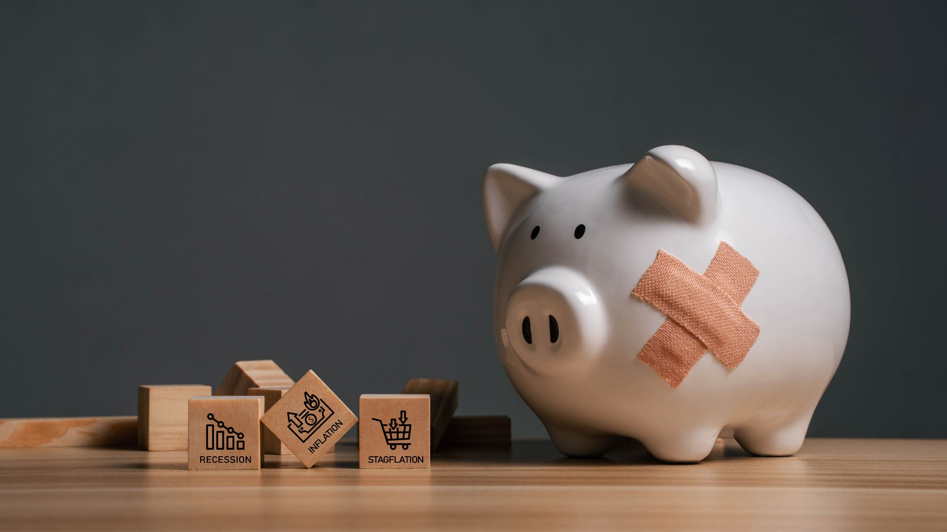 White piggy bank with a bandage and wooden blocks with financial icons.