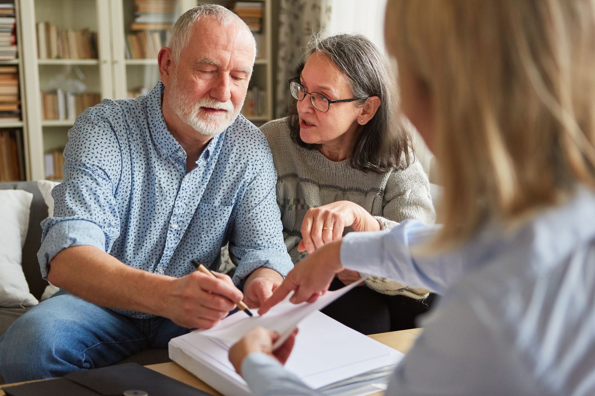 Older couple signs documents with advisor in a home setting.