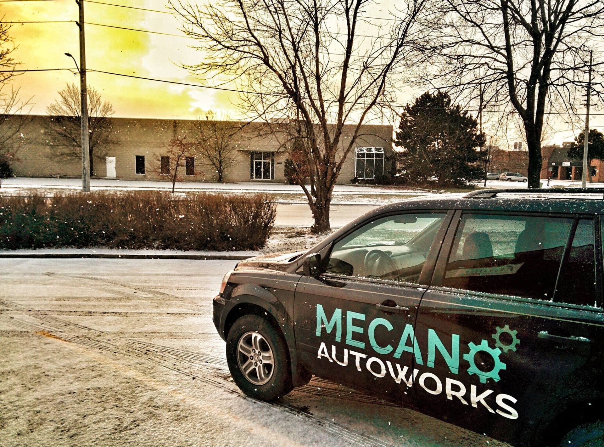 Black SUV with Mecano Autoworks logo parked in snowy lot, building in background. | Mecano Autoworks