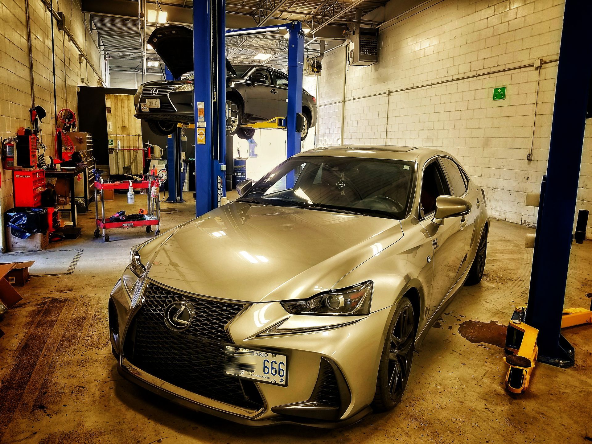 Silver Lexus sedan in an auto repair shop, another car elevated on a lift. | Mecano Autoworks