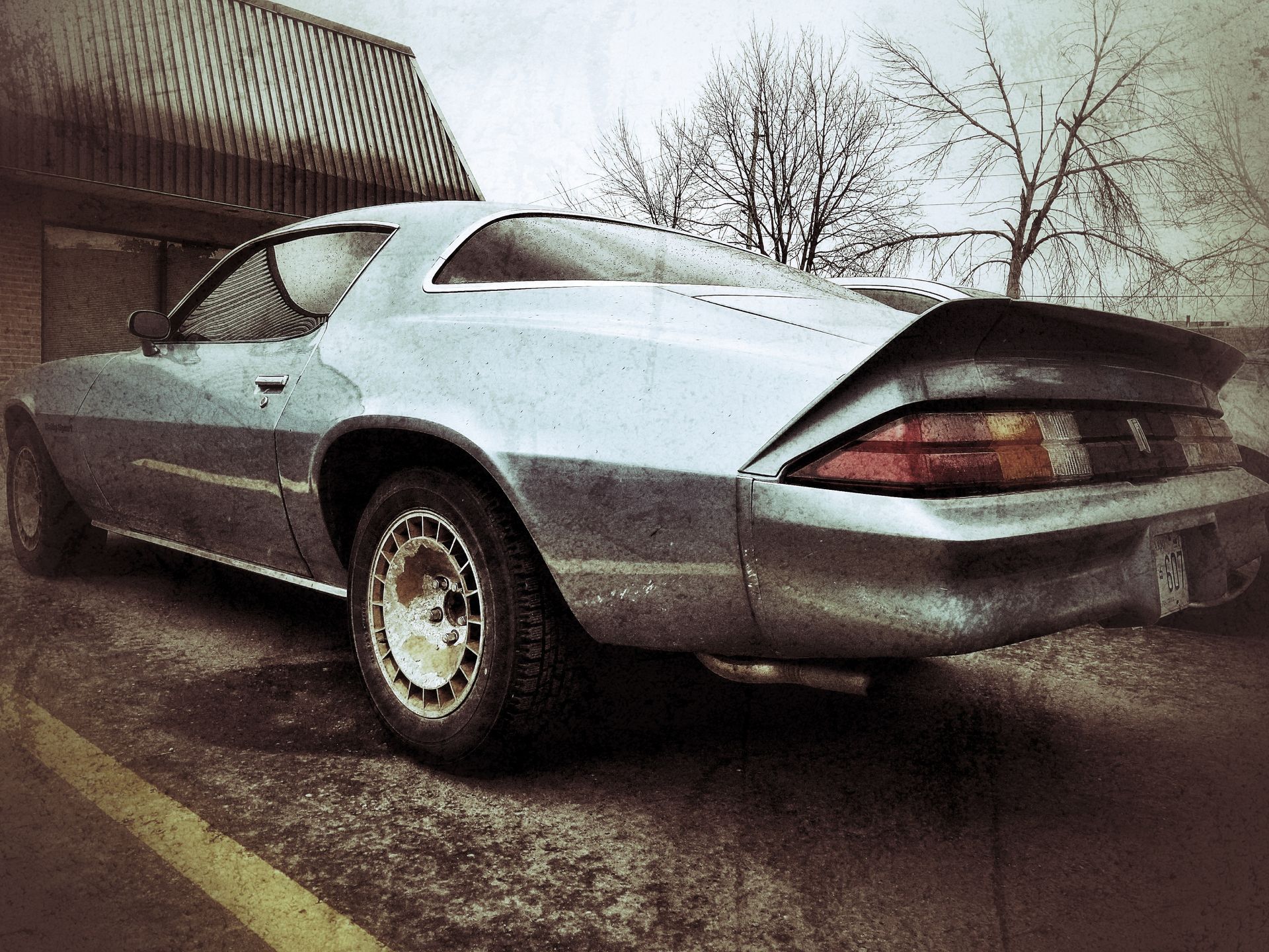Silver classic Camaro parked on a concrete surface next to a building.