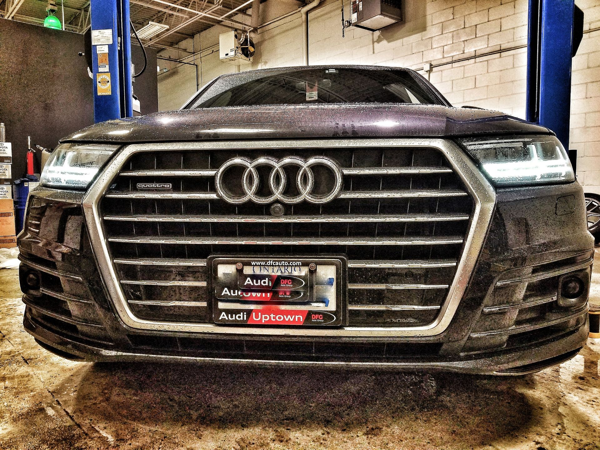 Dark Audi SUV in a repair shop, front view, raised on a lift.