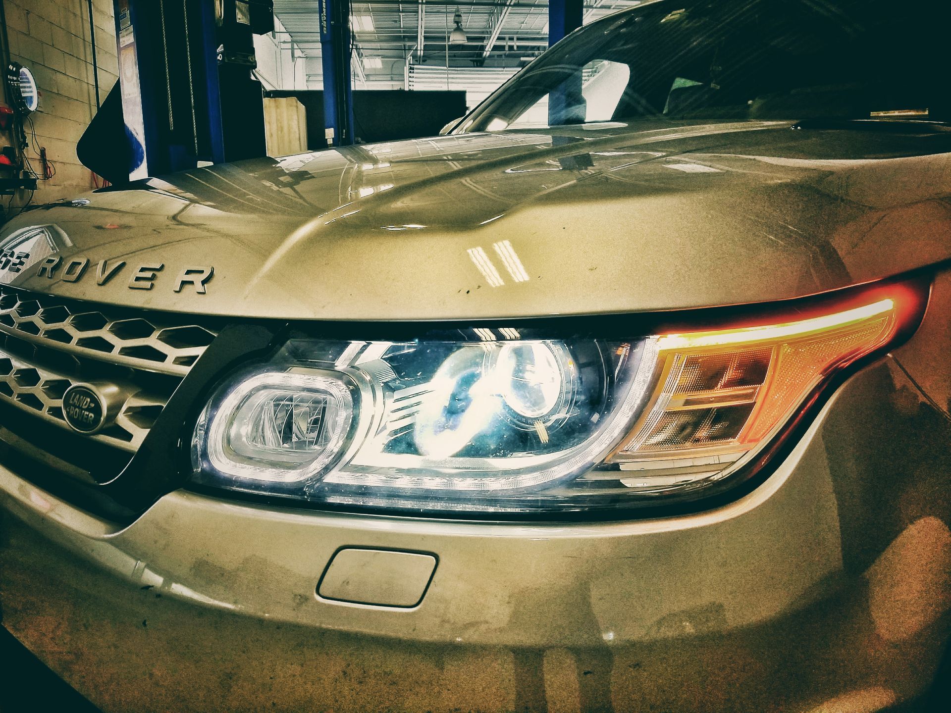 Silver Range Rover Sport, headlights on, parked indoors.
