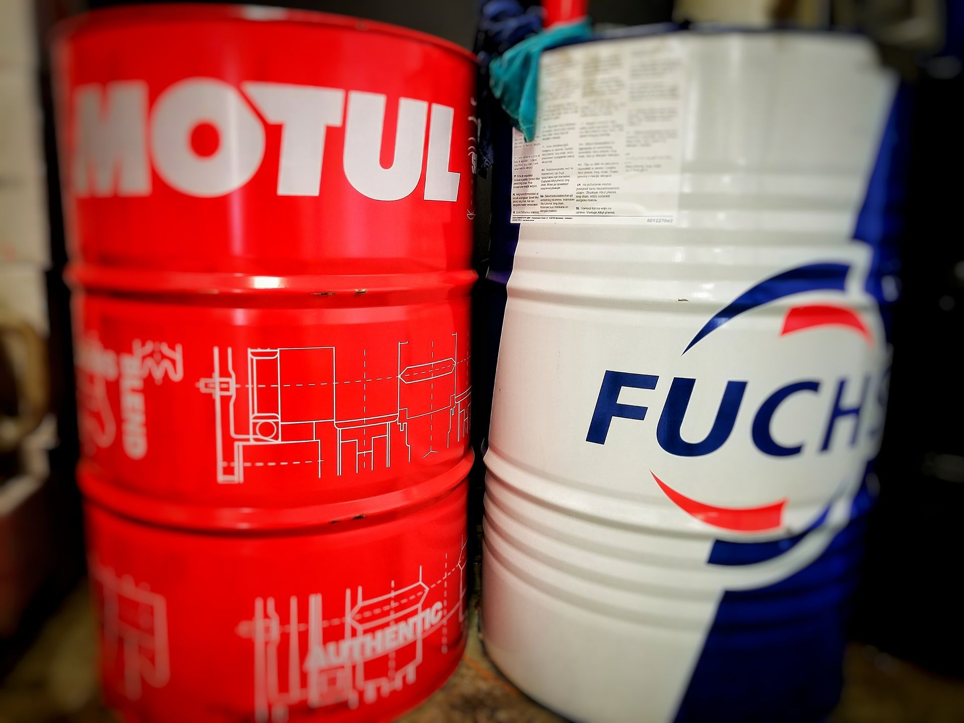 Red MOTUL and white FUCHS oil drums stacked side-by-side, for automotive use.
