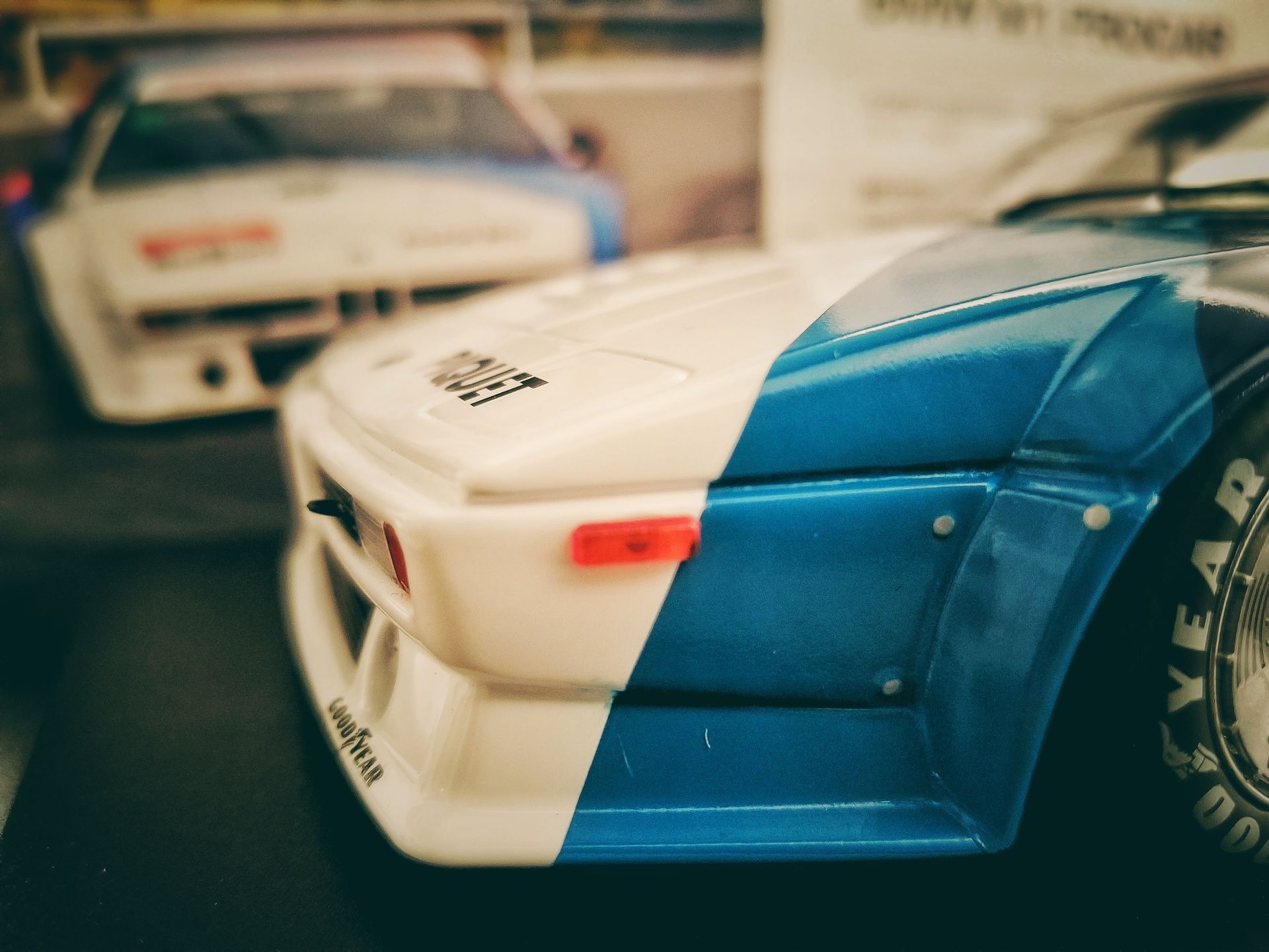 Close-up of a blue and white toy car with a blurred second car in the background.