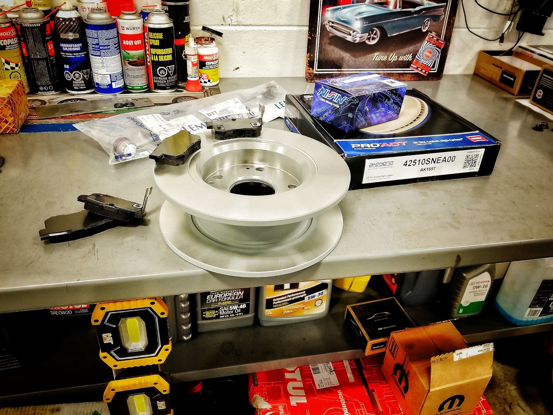 Brake parts on a workbench, including a rotor, pads, and other components in a garage setting.
