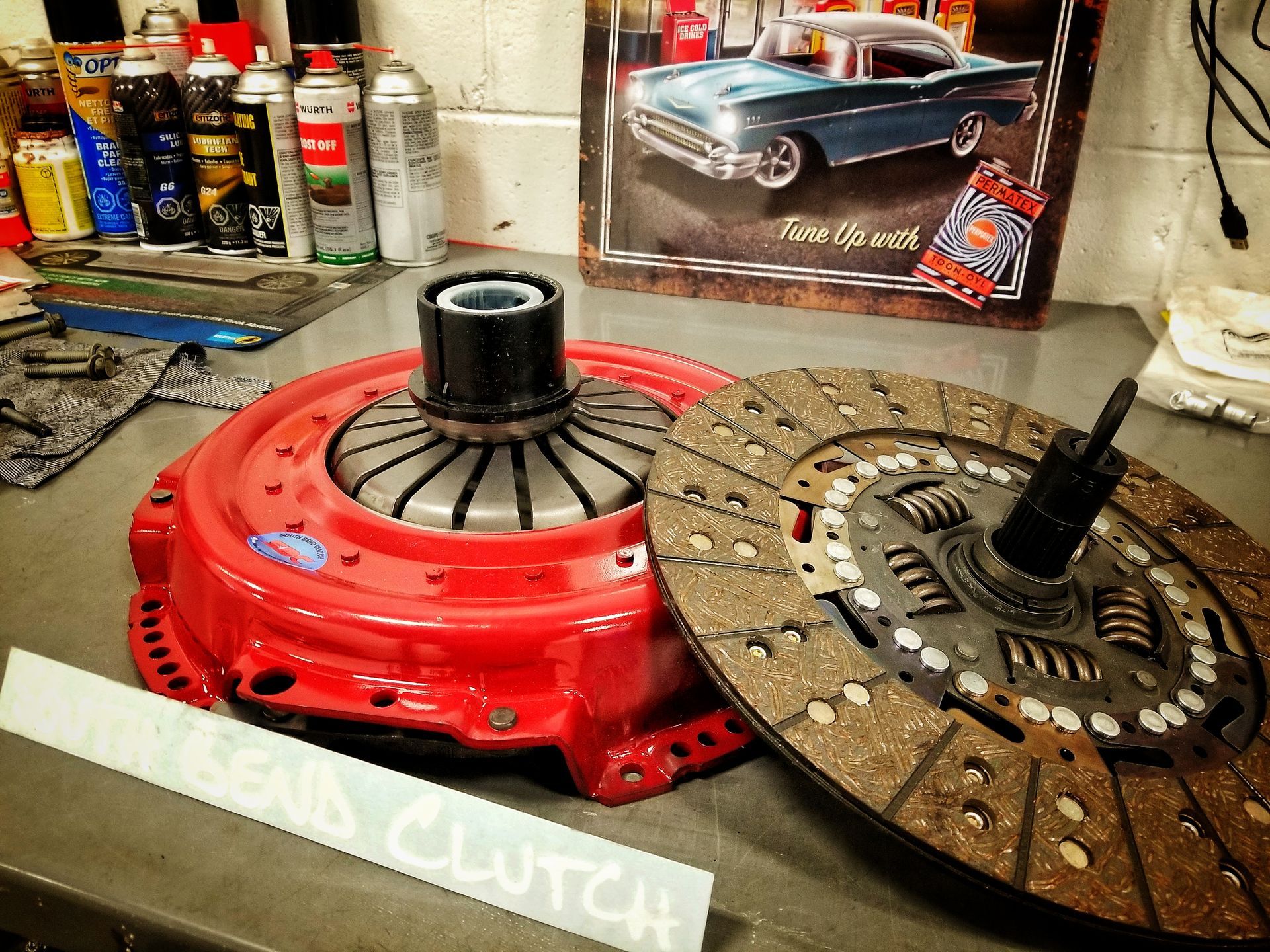 Red clutch assembly and clutch disc on a workbench, next to a car poster.