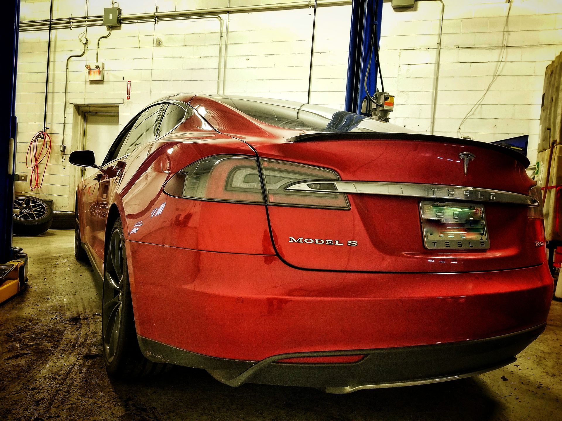 Red Tesla Model S in a garage, viewed from the rear.