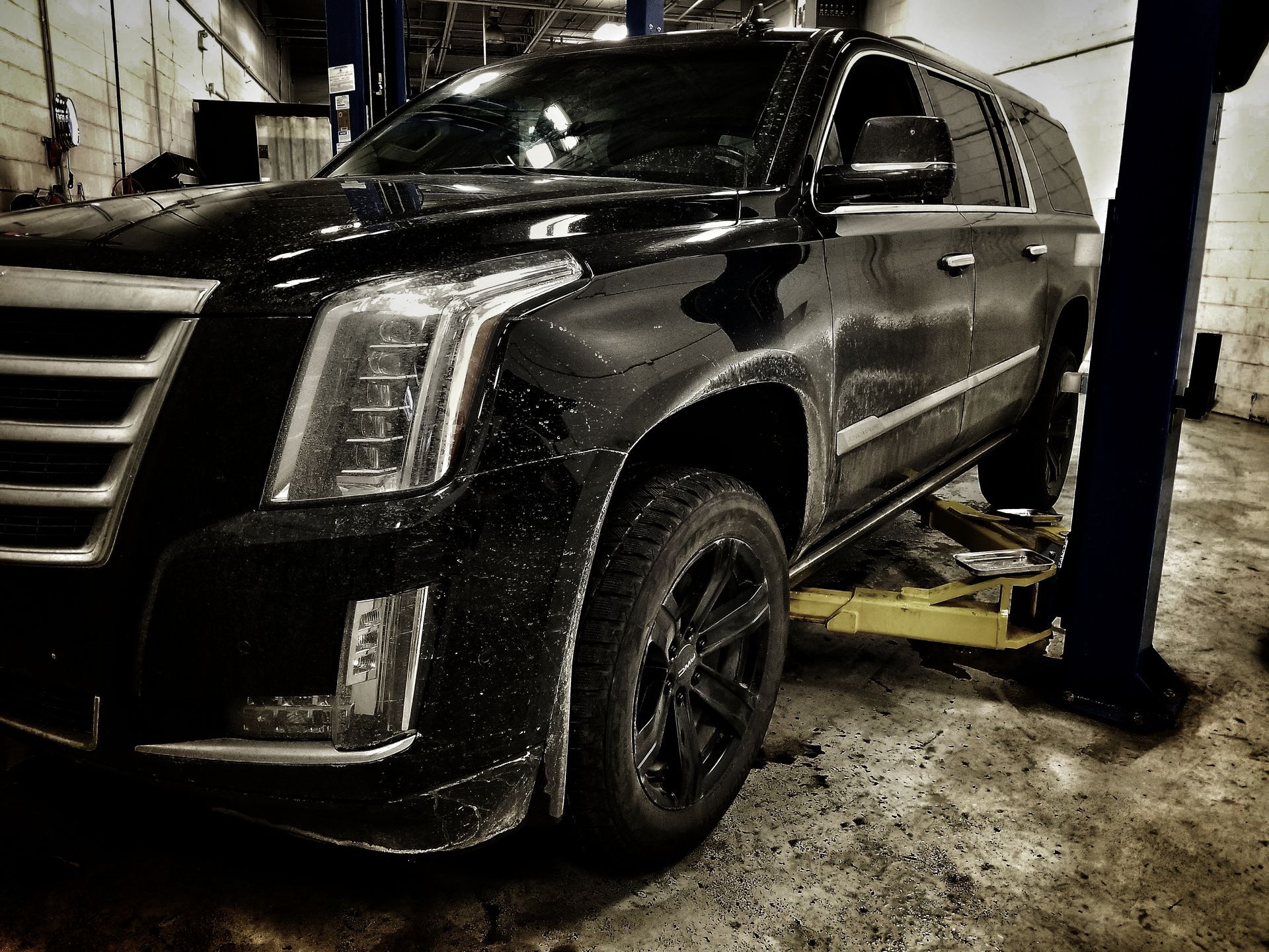Black Cadillac SUV on a lift in a garage.